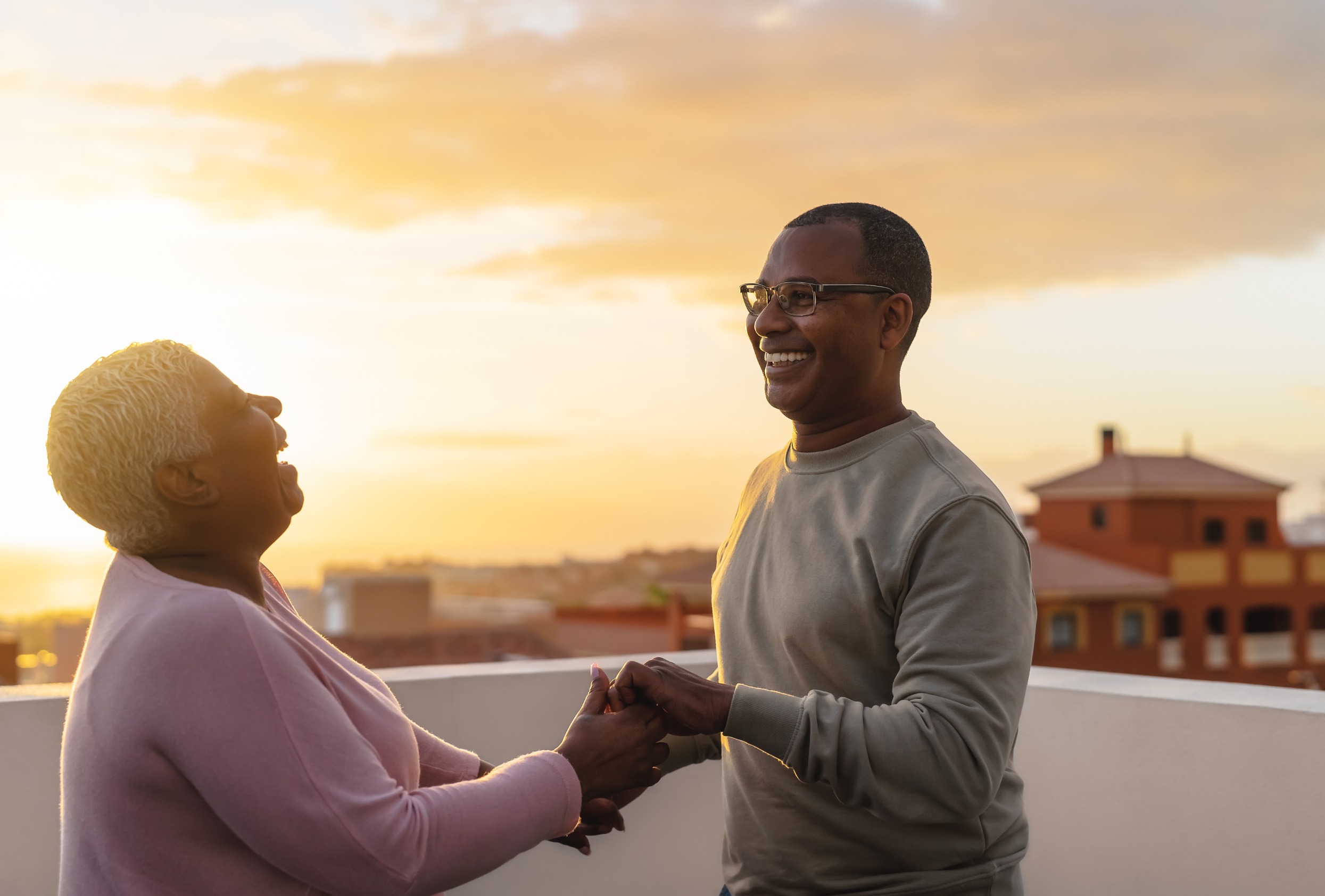 Happy Latin senior couple having romantic moment dancing on rooftop during sunset time.