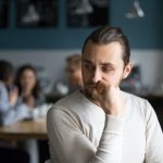 Middle aged man sits thoughtfully in a coffeeshop.